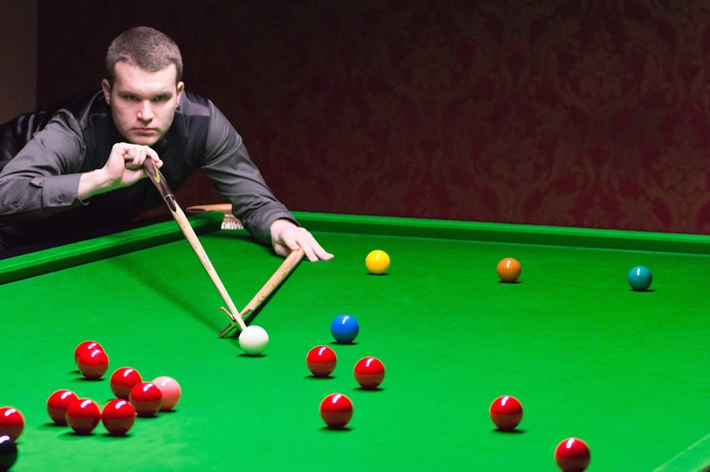 Snooker player leaning over table using rest to take shot